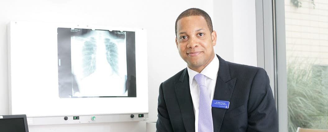 Professor Dean Fennell in a suit and tie, smiling and standing next to a chest x-ray.
