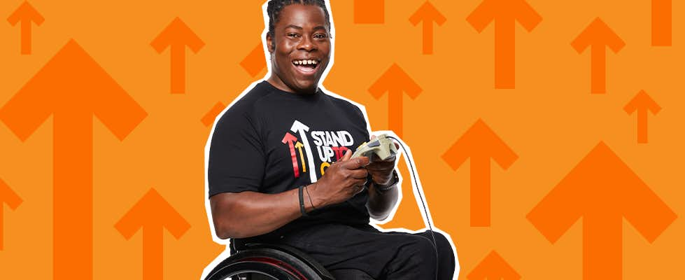 Paralympic athlete Ade Adepitan sitting in his wheelchair holding a game controller.