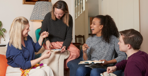 Four friends embroidering happily in a living room.