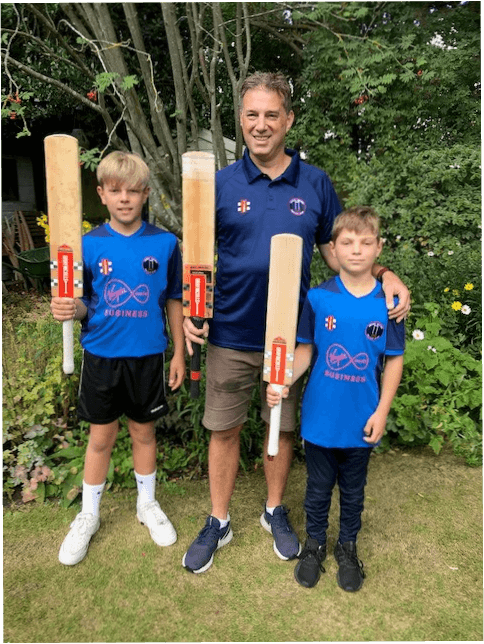Clint and his sons pose holding cricket bats in a garden.