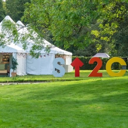 Picture of the famous white tent in Bake Off with Stand up to cancer logo sign in front.