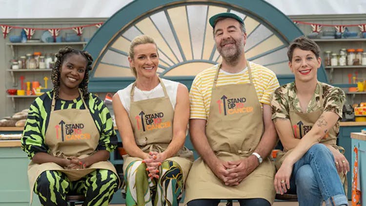 Oti Mabuse, Gabby Logan, David O’Doherty, and Suzi Ruffell in the Bake Off tent, smiling and wearing Stand Up to Cancer aprons.