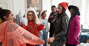 A room of people wearing eclectic clothes, including sunglasses indoors and a hat with a unicorn's horn on it.