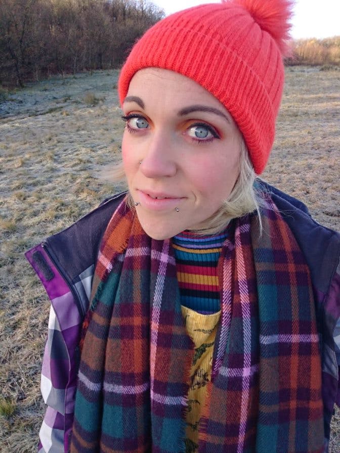 Emily taking a selfie in a frosty field while wearing a red hat and a scarf.