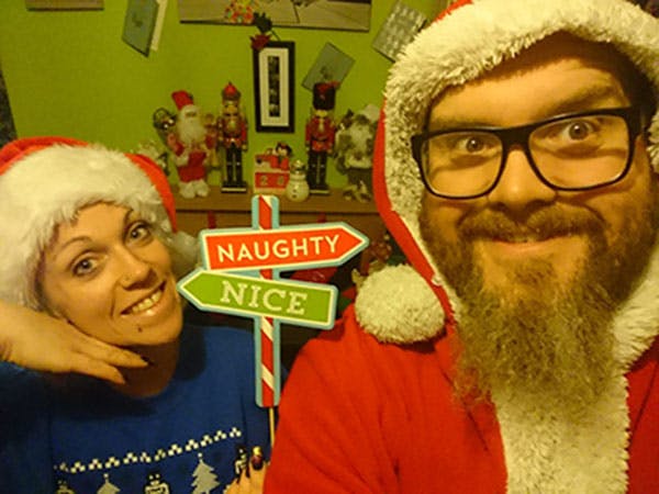 Emily takes a selfie with someone while wearing Christmas jumpers and hats with a sign saying naughty and nice.
