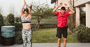 A man and a woman in active wear, jumping in a garden.