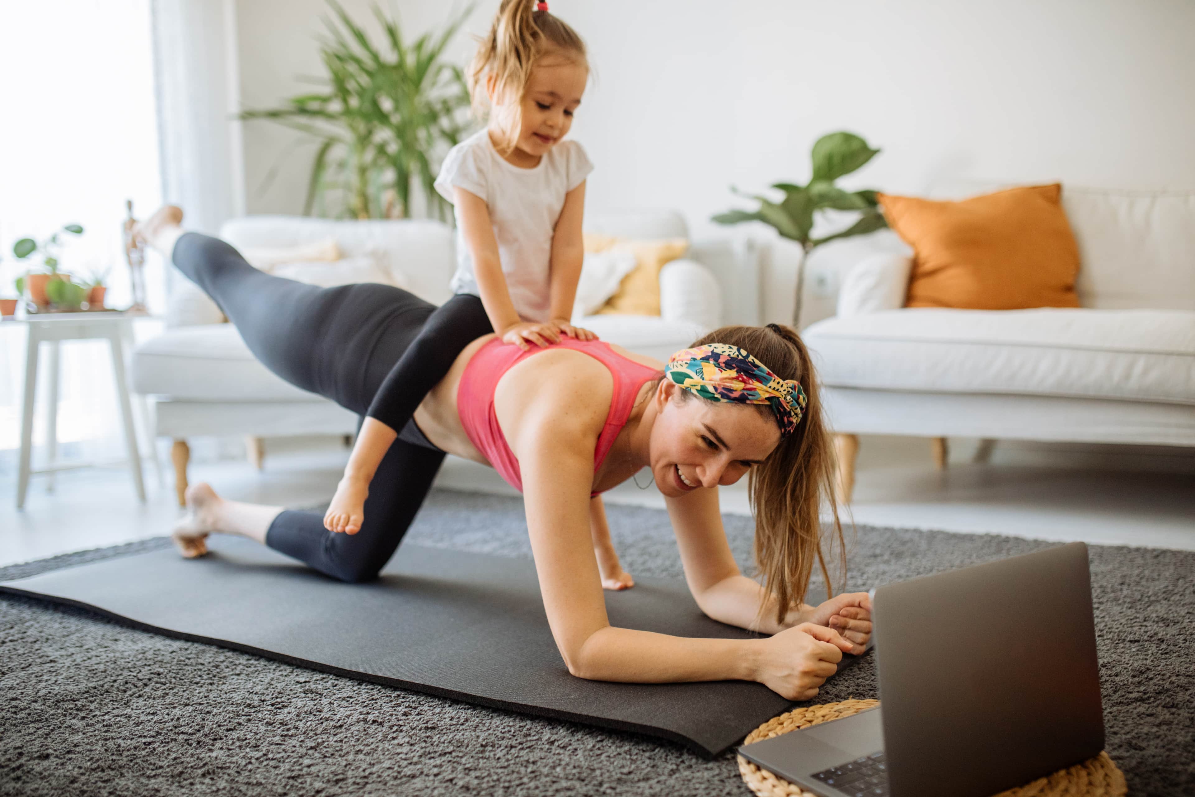 Woman doing a plank pose with child smiling on her back.