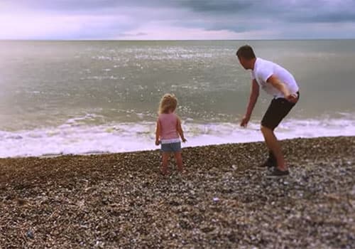 Brett and his daughter at the beach facing out to the sea.