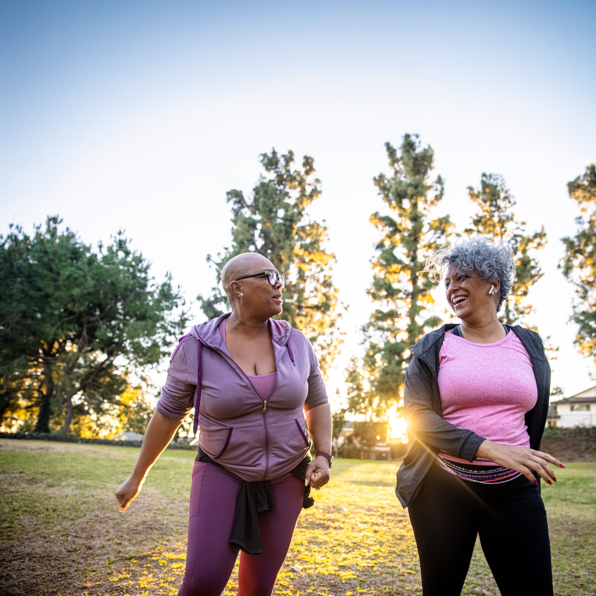 Two women walking through a park smiling at each other.