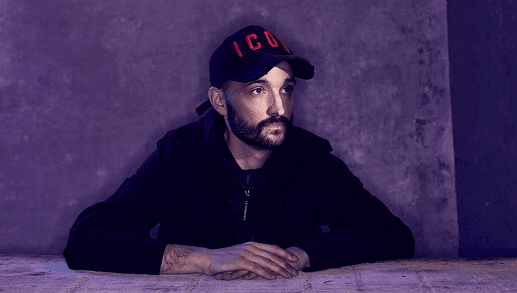 Tom Parker is looking at something in the distance. He is wearing a black hoodie with a baseball cap.