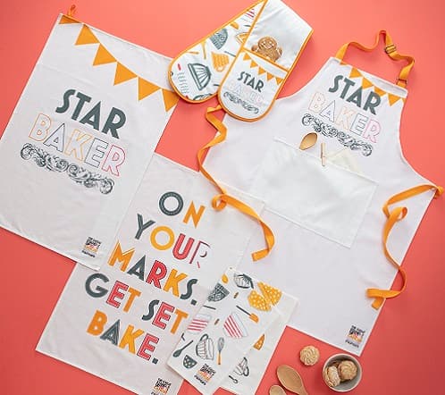 Star baker merchandise displayed on a red background, including an apron, oven gloves and posters.