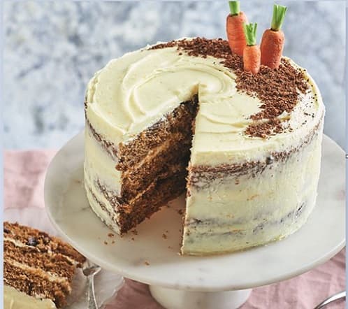 A carrot cake with a slice taken out of it and 3 little carrots stuck into the top.